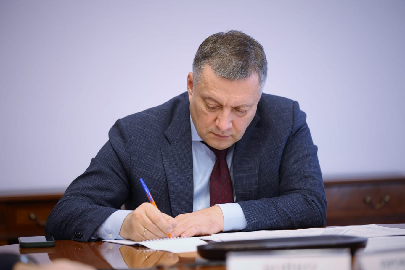 Человек в костюме пишет на бумаге за столом.