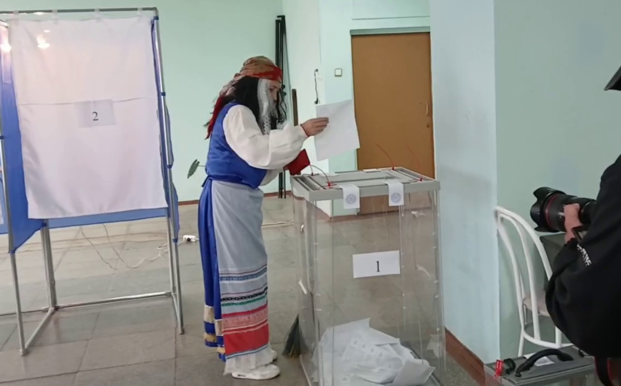 Человек в костюме голосует на избирательном участке.
