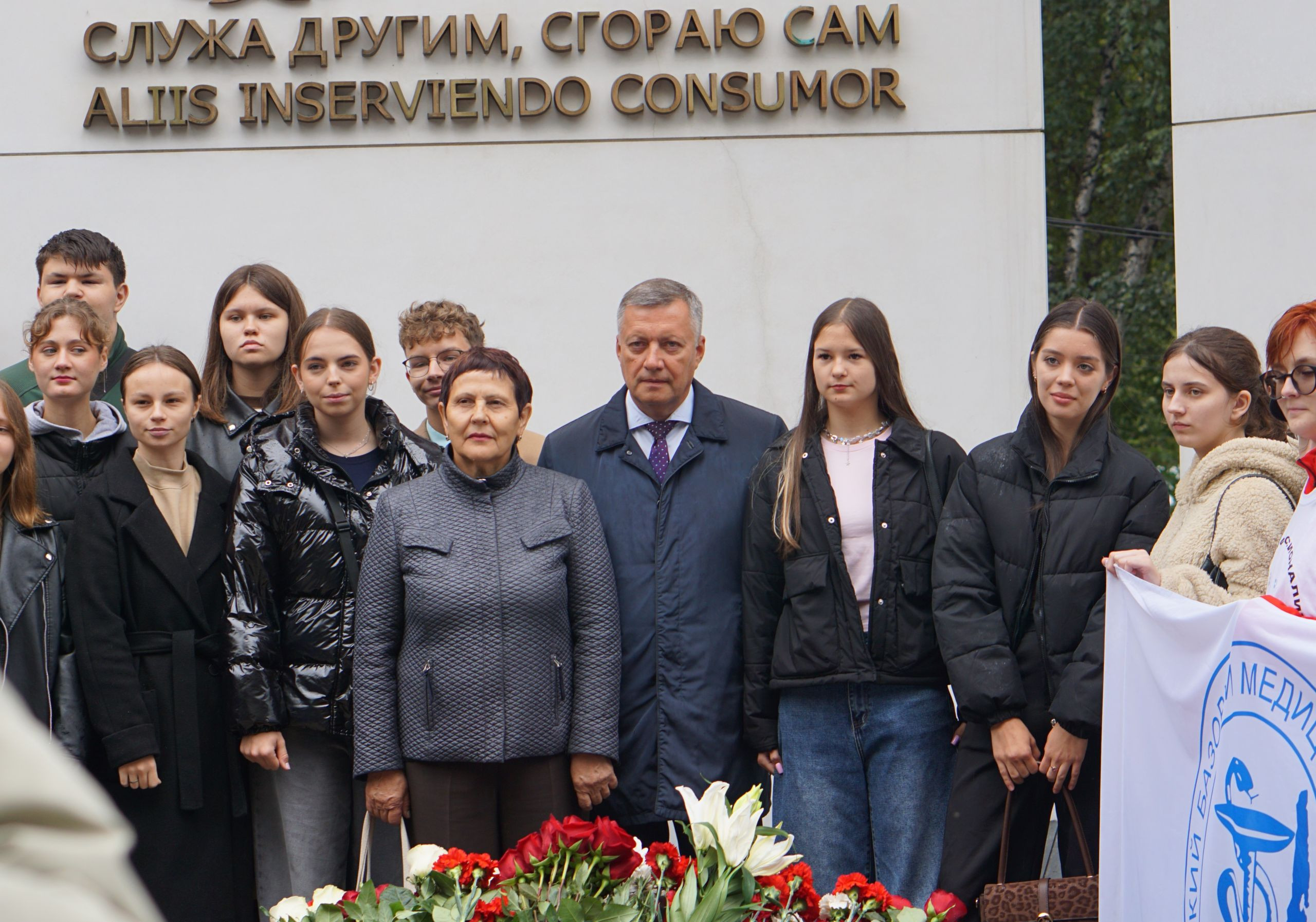 Группа людей перед мемориалом с фразой на латыни.