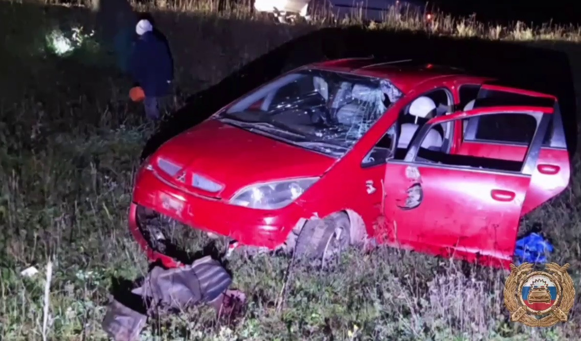 Разбитый красный автомобиль на обочине дороги ночью.