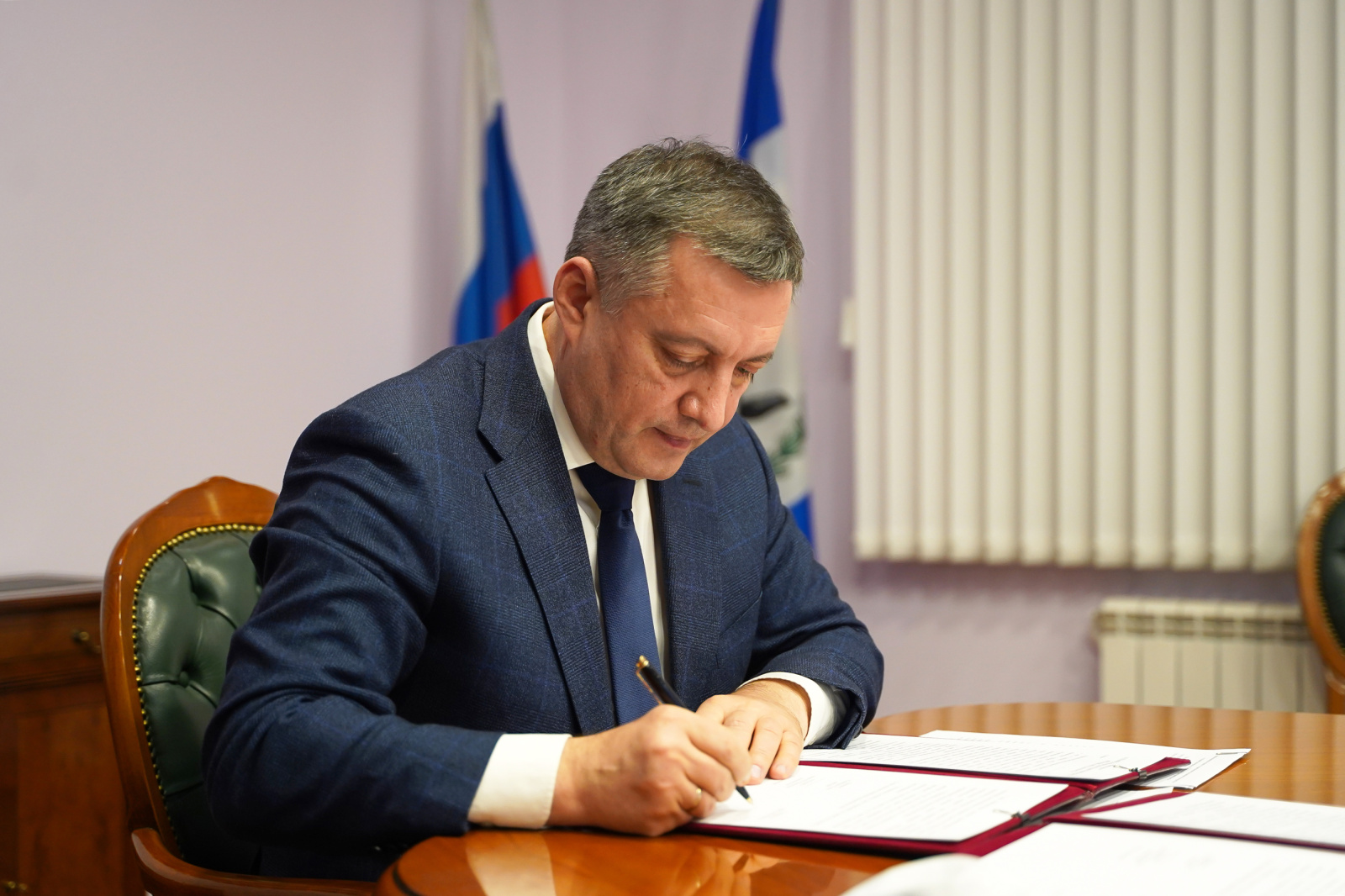 Мужчина подписывает документы, российский флаг на заднем плане.