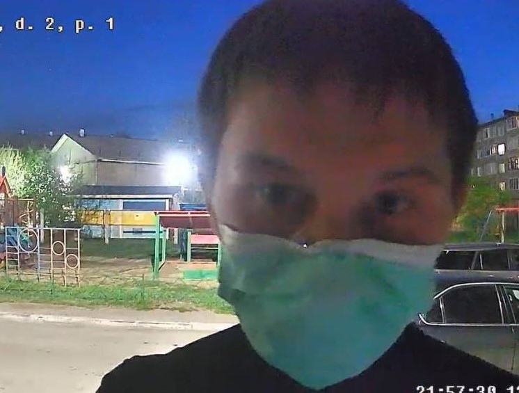 Человек в медицинской маске ночью на фоне жилых домов и детской площадки.