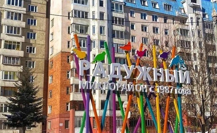 Цветная вывеска Радужный на фоне жилых домов.
