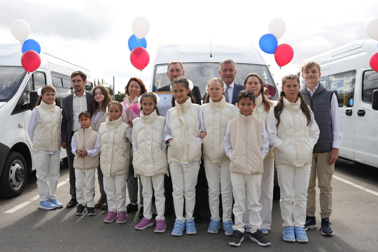 Группа людей перед белыми микроавтобусами с шарами.
