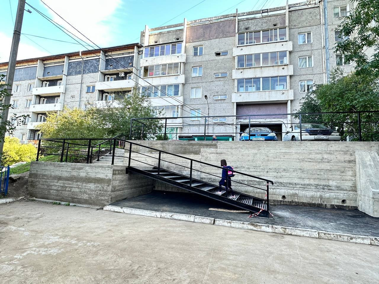 Девочка поднимается по металлическому пандусу к зданию.