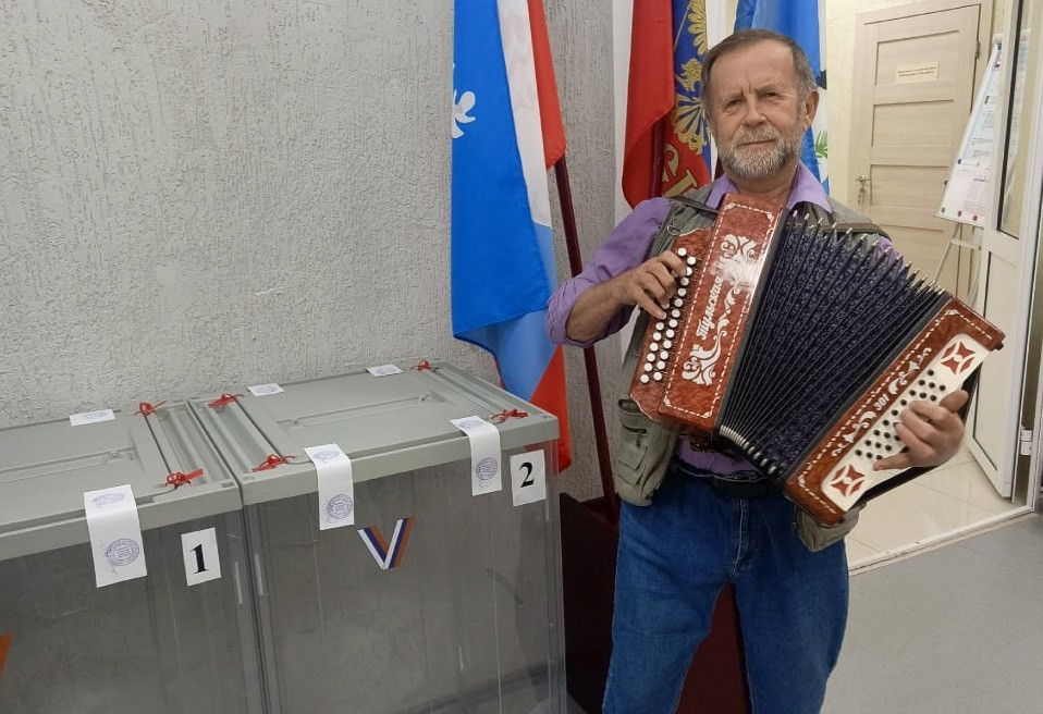 Человек с аккордеоном у избирательных урн и флагов.
