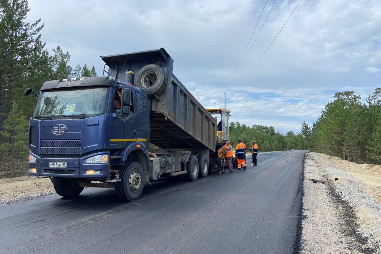 Грузовик и рабочие укладывают асфальт на дороге.