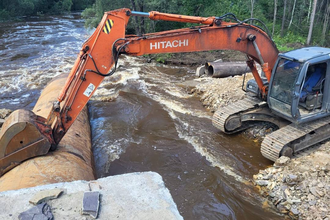 Трактор устанавливает трубу в реку