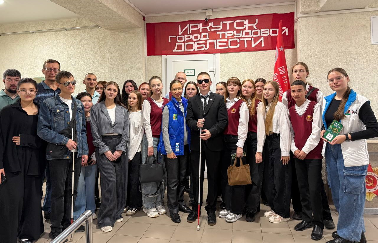 Группа людей в помещении с красным транспарантом.