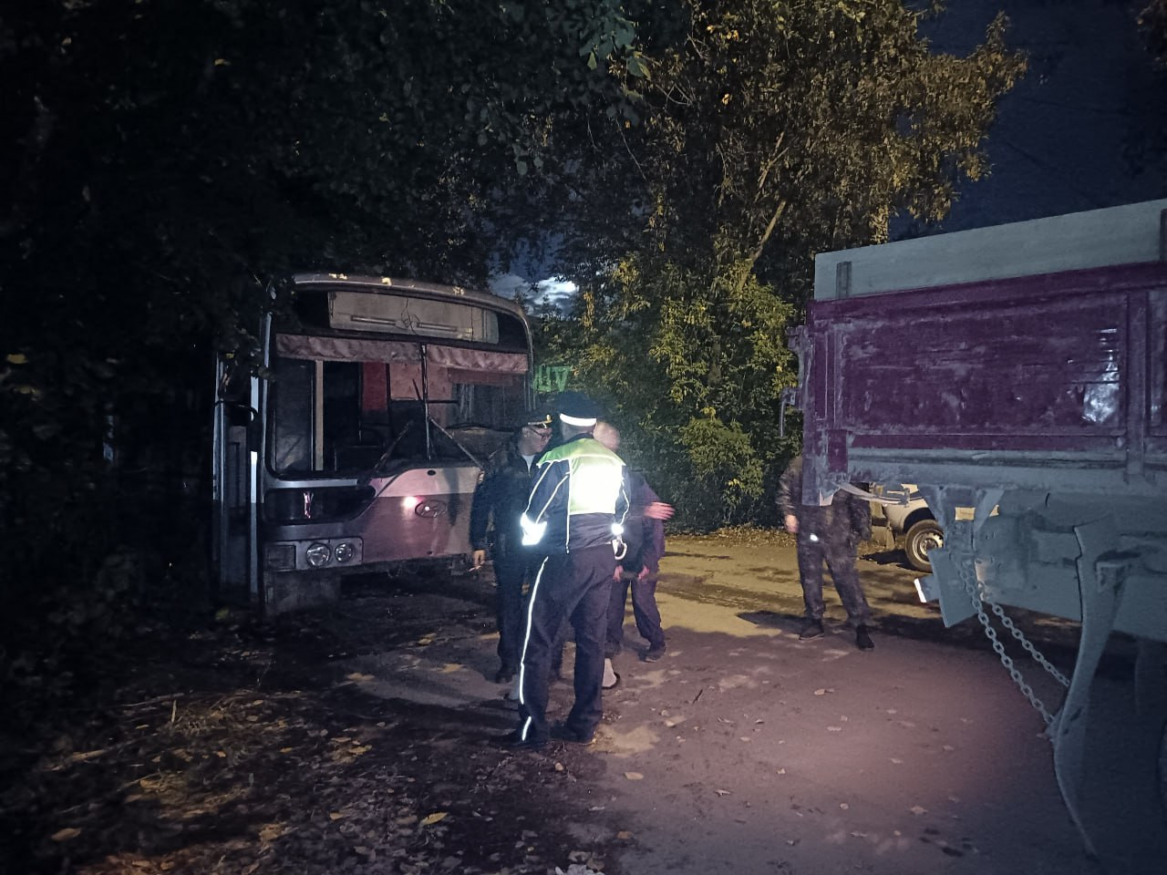 Полиция осматривает аварию автобуса и грузовика ночью.