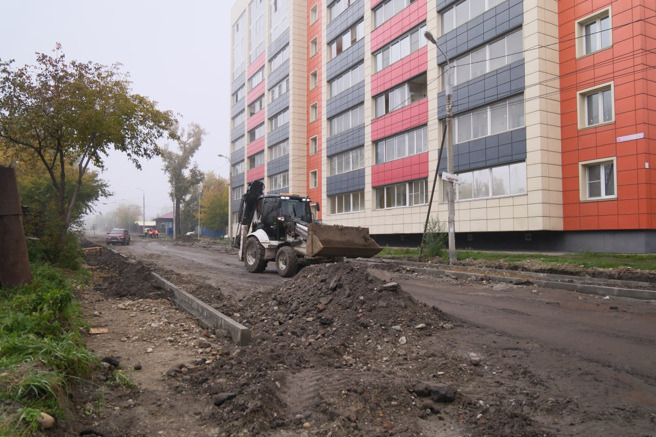 Дорожные работы у жилого дома, трактор в действии.