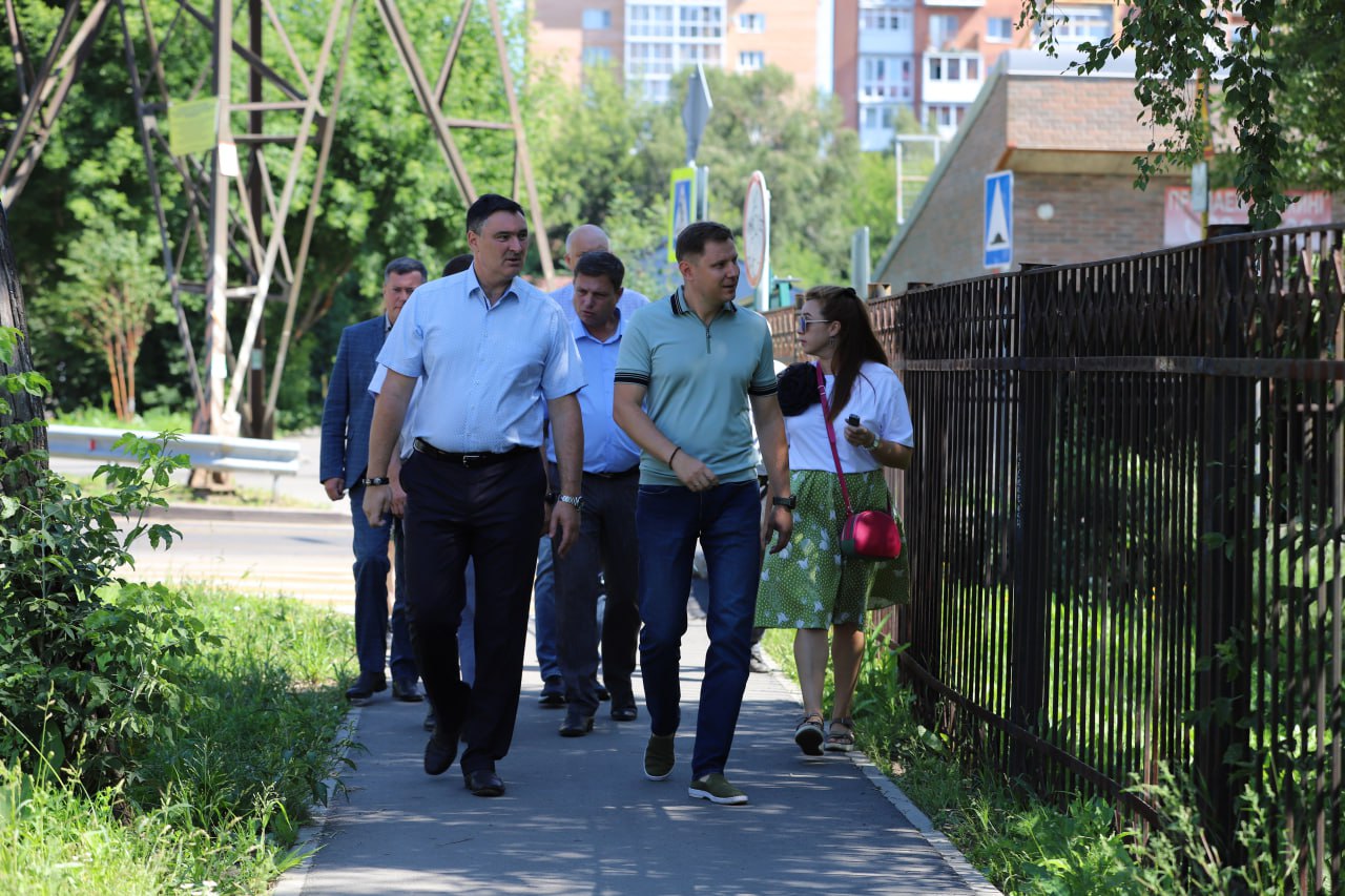 Группа людей на тротуаре среди зелени.