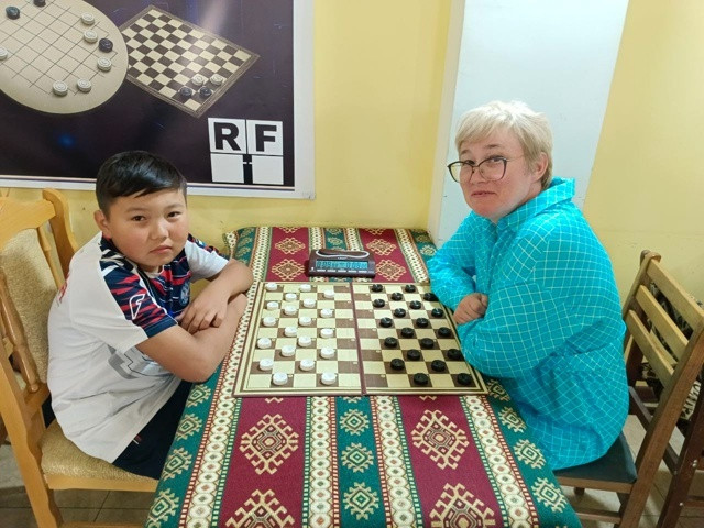 Два человека играют в шашки в помещении.