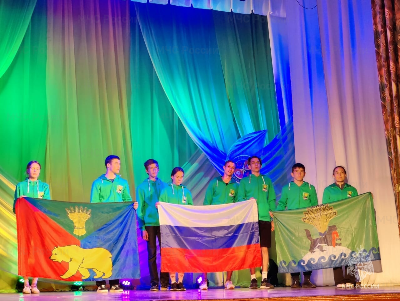 Участники с флагами на сцене на светлом фоне.
