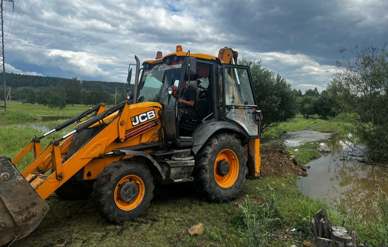 Экскаватор JCB на зеленом лугу после дождя