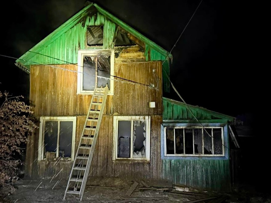 Обгоревший дом ночью с лестницей возле окна.