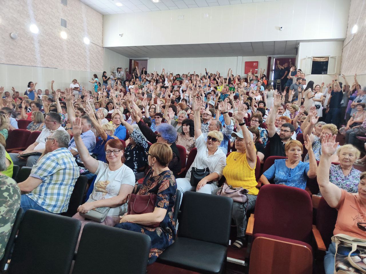 Люди на собрании поднимают руки в зале.