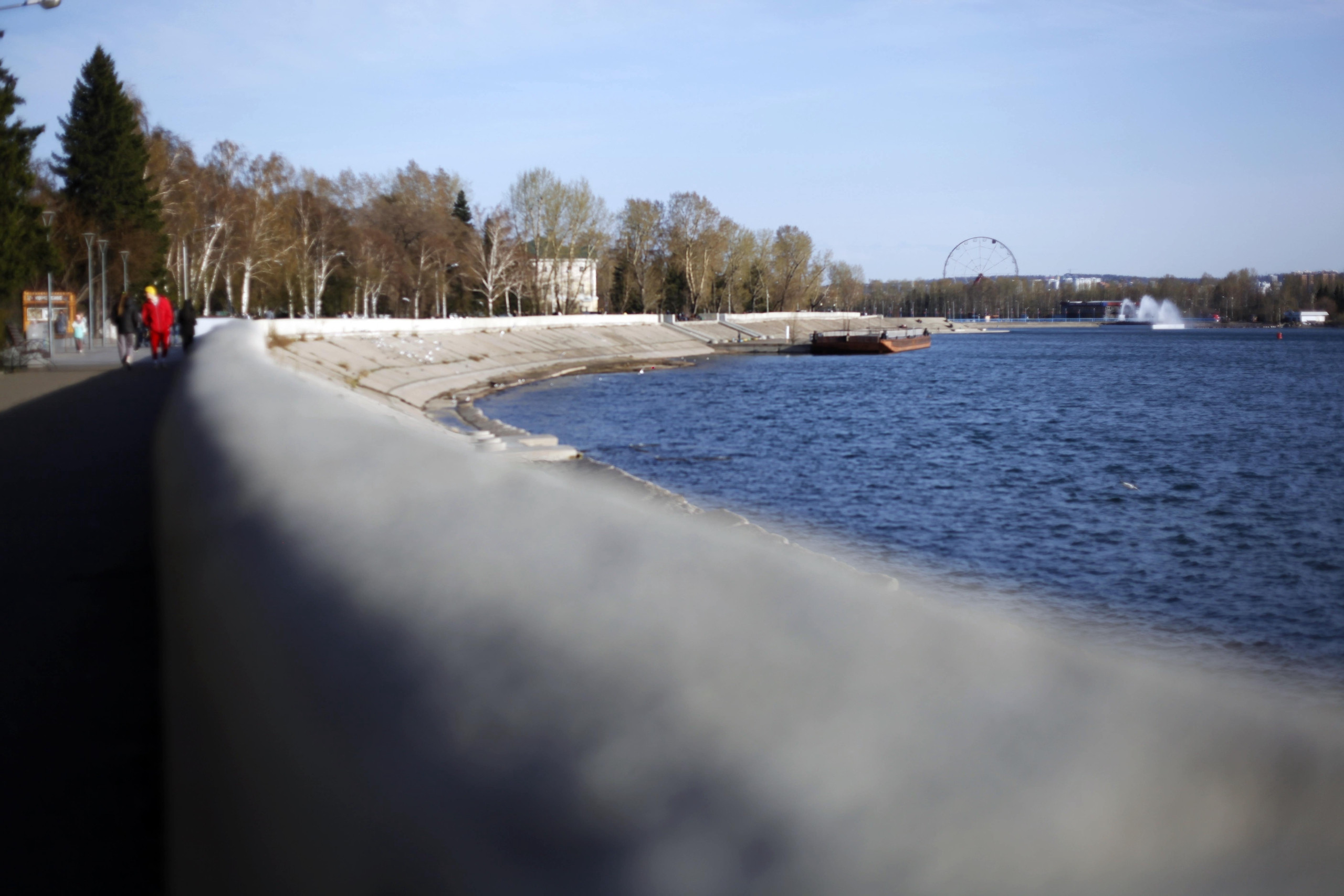 Набережная реки с прохожими и деревьями весной.