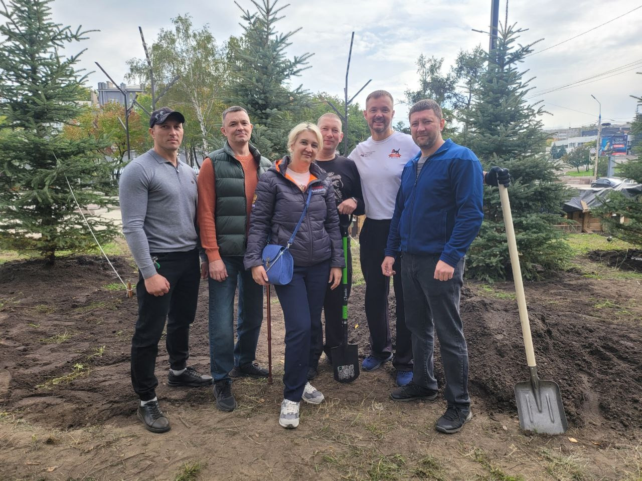 Группа людей на субботнике с деревьями и лопатами.